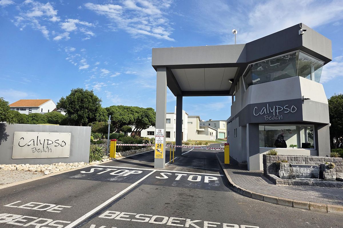 The entrance to Calypso Beach estate featuring a modern security gatehouse, boom gate access control, and paved driveway.