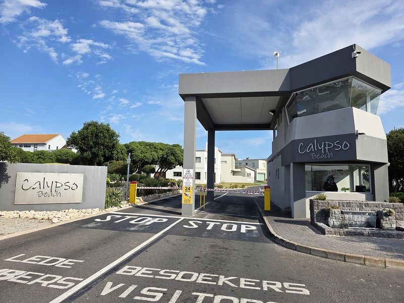 The entrance to Calypso Beach estate featuring a modern security gatehouse, boom gate access control, and paved driveway.
