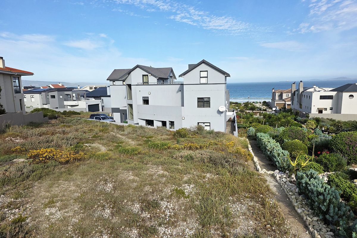 A view of the rear elevation of a modern residential property, featuring landscaped garden areas and proximity to the coastline.
