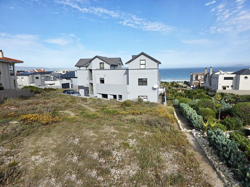 A view of the rear elevation of a modern residential property, featuring landscaped garden areas and proximity to the coastline.