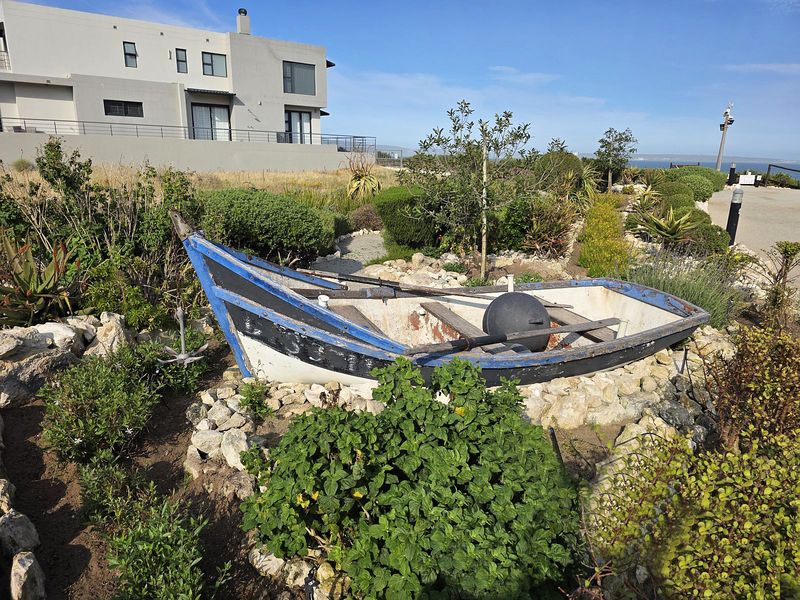 A landscaped garden area featuring a decorative boat feature, rockery, and established shrubs, set against a modern residential building.