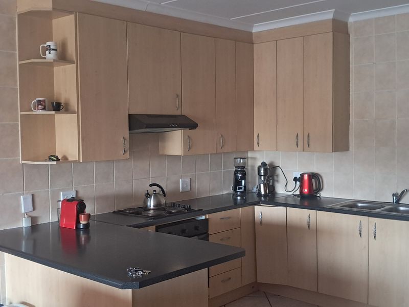 A functional kitchen featuring light wood-finish cabinetry, dark laminate countertops, a breakfast bar, and tiled backsplash with integrated oven and extractor fan.