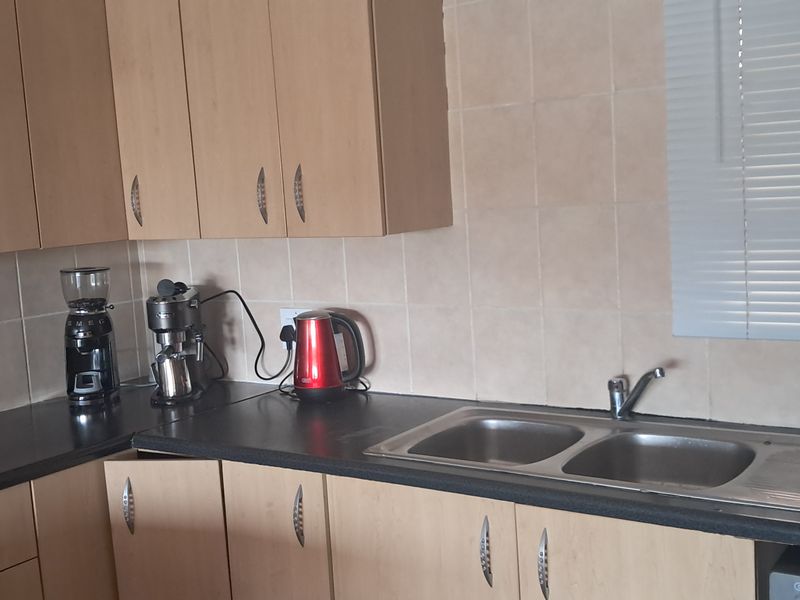 A functional kitchen featuring light wood-finish cabinetry, dark laminate countertops, a double stainless steel sink, and tiled splashbacks.