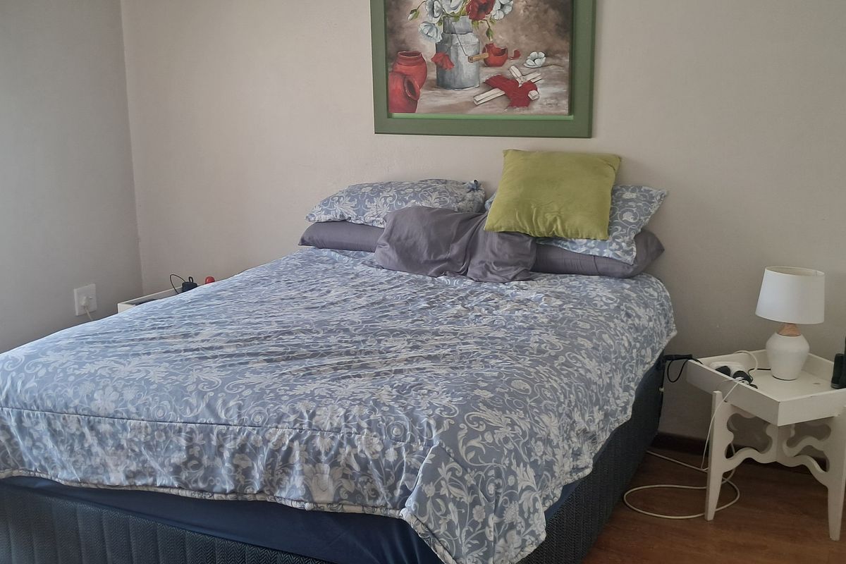 A functional bedroom featuring laminate flooring, a built-in wardrobe, and natural light provided by a window with venetian blinds.