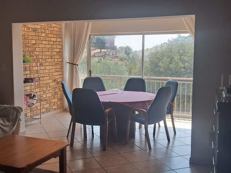 Open plan living and dining area featuring tiled floors, an exposed brick feature wall, and large sliding doors leading to a balcony with scenic views.