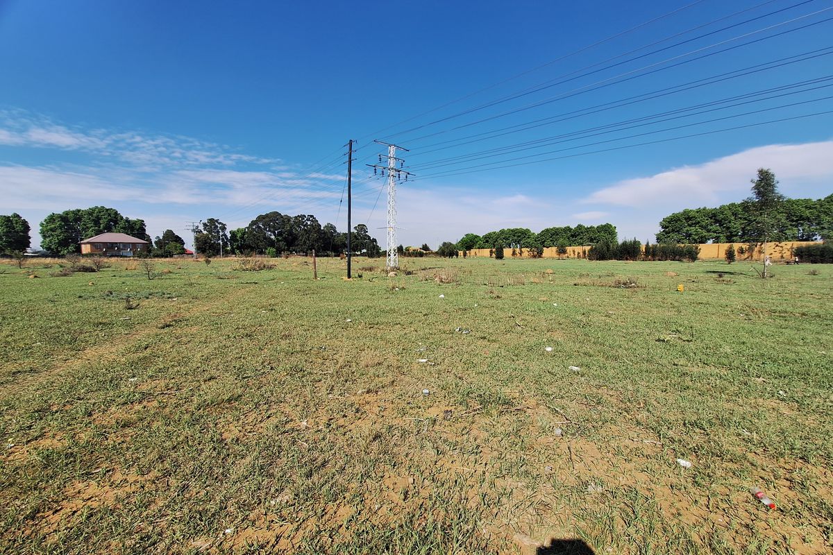 A wide-angle view of a vacant residential plot featuring open grassland and overhead power lines.