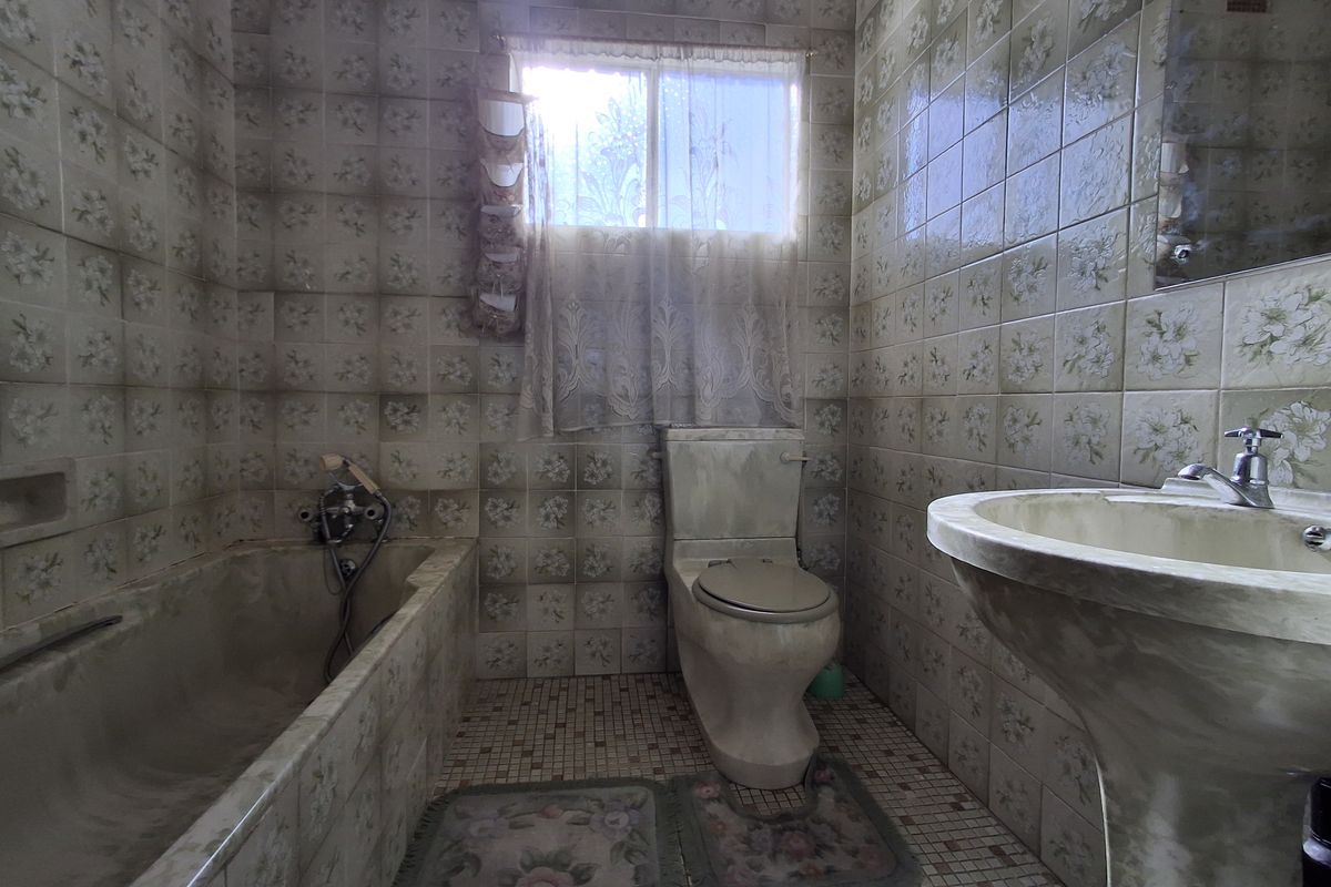 A dated bathroom featuring original floral ceramic wall tiles, a pedestal basin, and a built-in bathtub, requiring significant modernization and refurbishment.