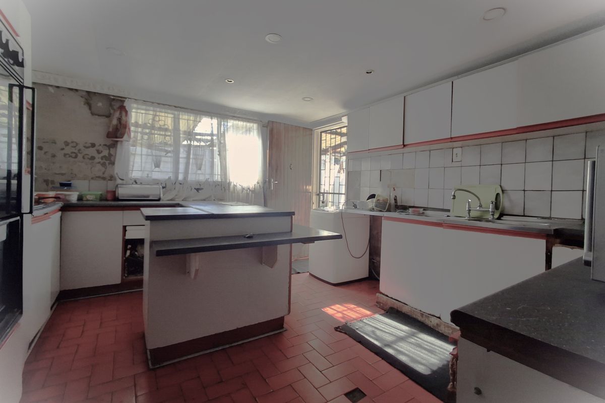 A dated kitchen featuring a central island, tiled flooring, and white cabinetry, currently requiring significant renovation and repair to the wall finishes and fixtures.