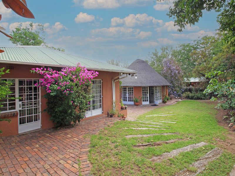 Rear view of the farm property featuring a thatched roof structure, brick paved patio area, and established garden surroundings.