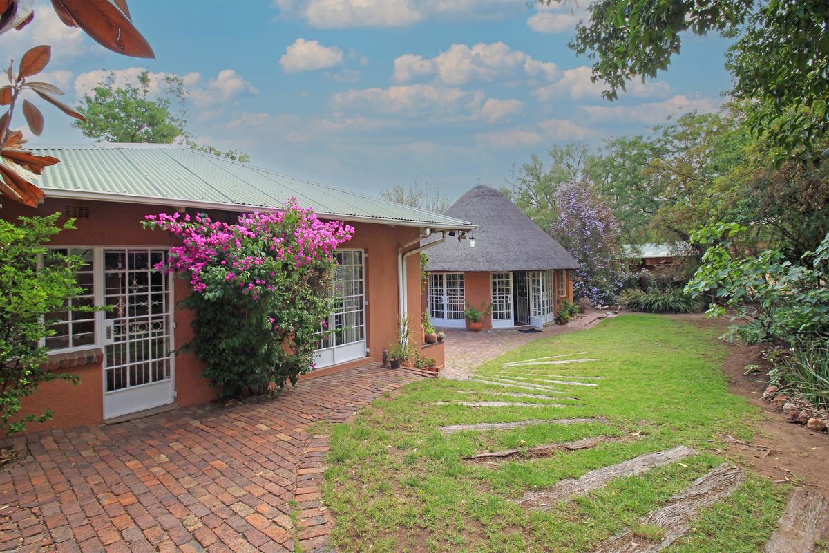 Rear view of the farm property featuring a thatched roof structure, brick paved patio area, and established garden surroundings.