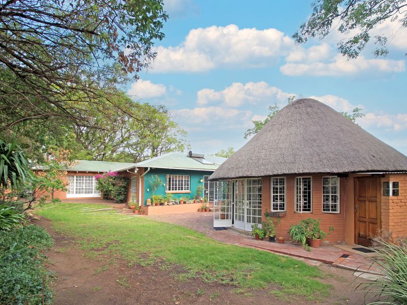 Rear view of the farm property featuring a traditional thatched roof structure, brick exterior, and paved courtyard area surrounded by established trees.