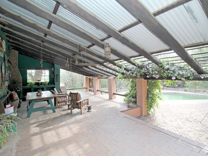 Spacious covered patio featuring a rustic timber beam roof, brick paving, and a built-in counter, overlooking the adjacent swimming pool area.