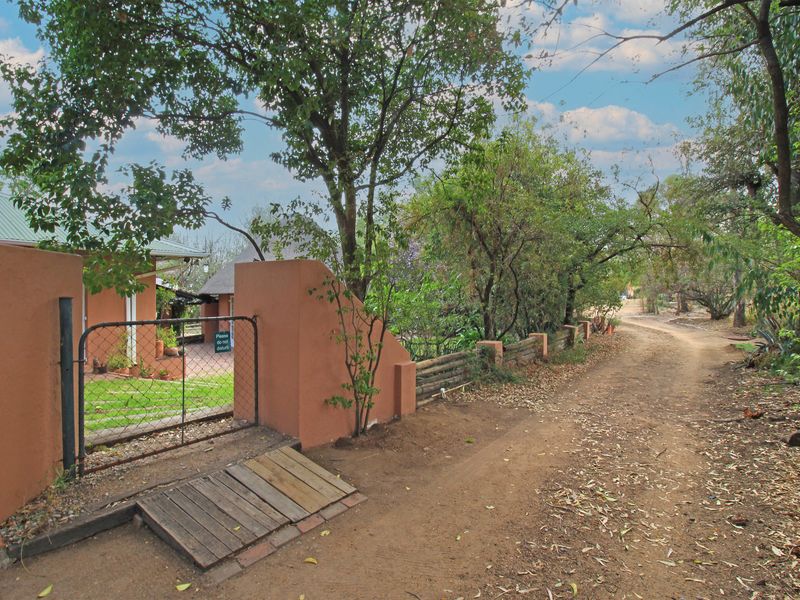 A rustic farm entrance featuring a dirt driveway, masonry boundary wall, and a metal gate leading to the property.