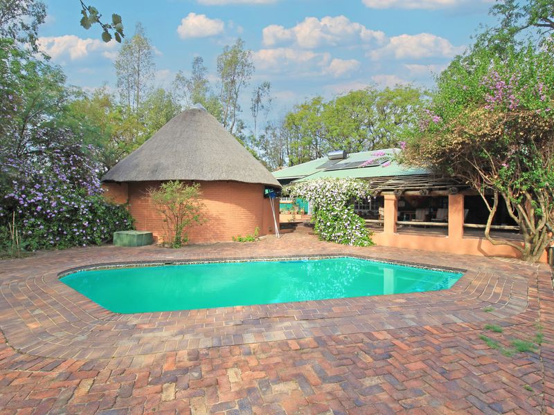 Outdoor pool area featuring brick paving, a traditional thatch-roof structure, and a covered patio space set within a landscaped garden environment.