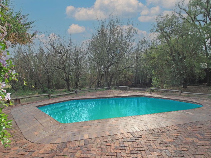 Outdoor swimming pool area featuring brick paving surround and rustic timber post fencing, set against a natural wooded backdrop.