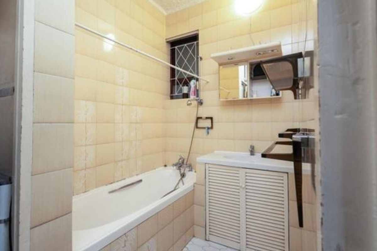 A dated bathroom featuring a built-in bathtub with shower attachment, a vanity basin with storage cabinet, and wall-mounted mirror cabinet.