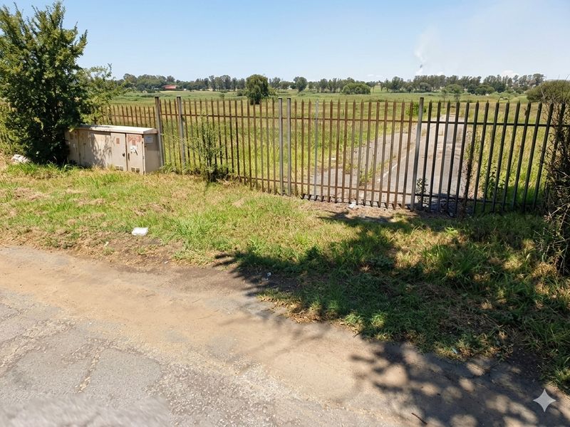 A view of the vacant residential land featuring steel palisade fencing and an electrical utility box along the perimeter.