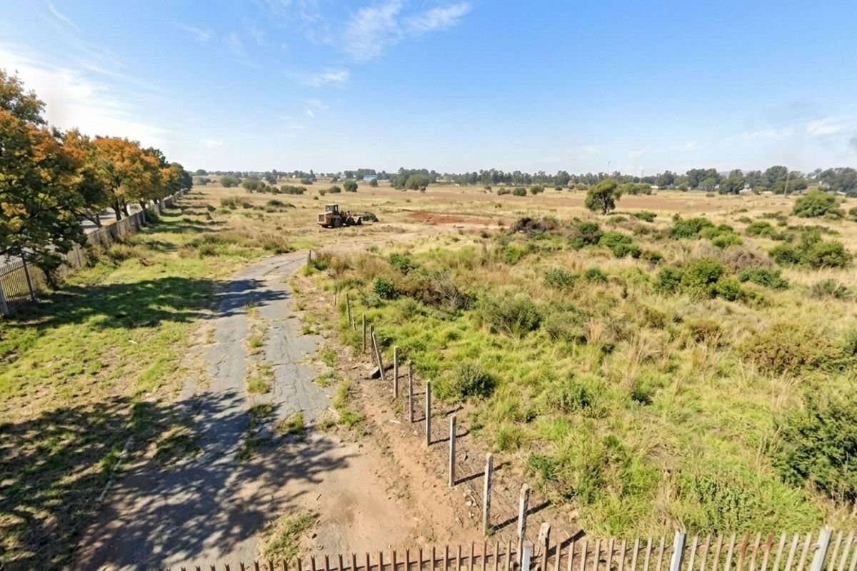 An aerial view of a large, undeveloped residential land parcel featuring perimeter fencing and an unpaved access road.