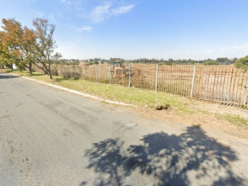 Street view of a vacant residential plot featuring a metal palisade fence and direct road access.