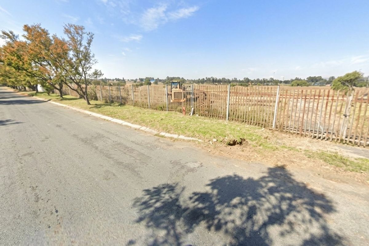 Street view of a vacant residential plot featuring a metal palisade fence and direct road access.