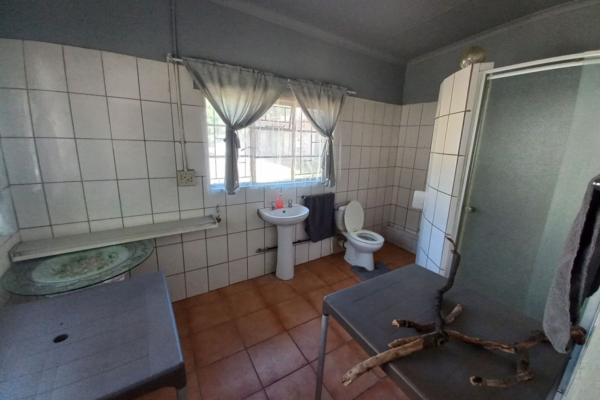 A functional bathroom featuring a pedestal basin, toilet, and shower enclosure with tiled walls and flooring, offering potential for modernization.