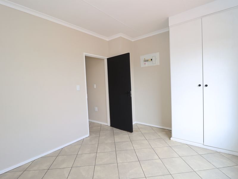 A clean, empty bedroom featuring neutral wall tones, tiled flooring, and a built-in white wardrobe with a modern black door.