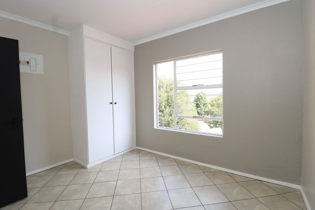 A clean, empty bedroom featuring neutral wall tones, tiled flooring, and a built-in cupboard with natural light from the window.