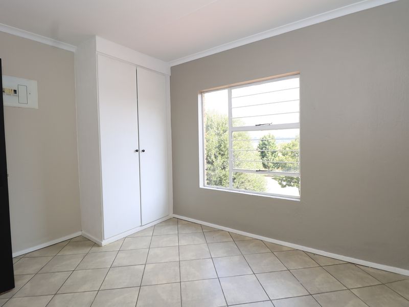 A clean, empty bedroom featuring neutral wall tones, tiled flooring, and a built-in cupboard with natural light from the window.