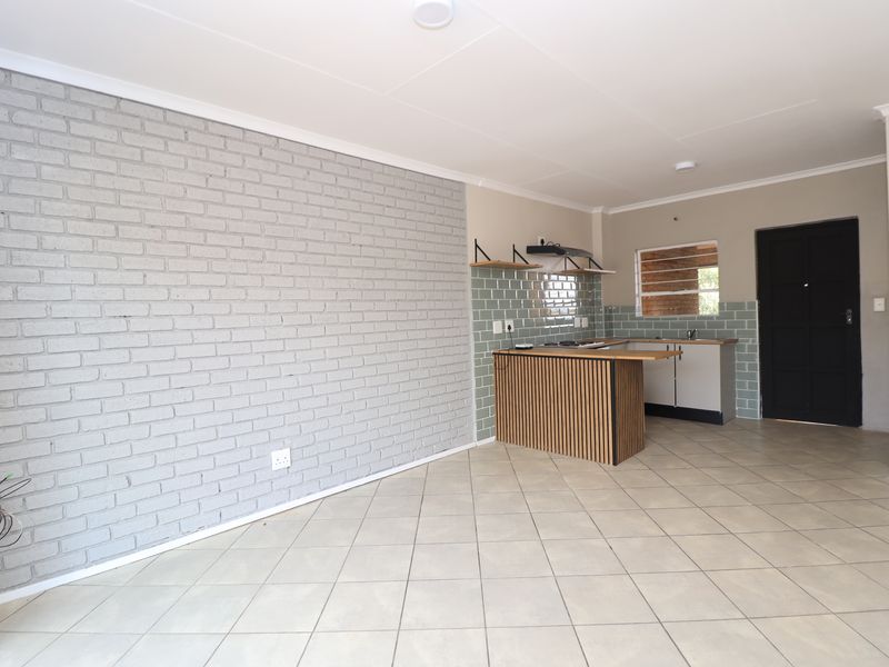 An open-plan living and kitchen area featuring a grey exposed brick feature wall, tiled flooring, and a modern kitchen with a breakfast island.