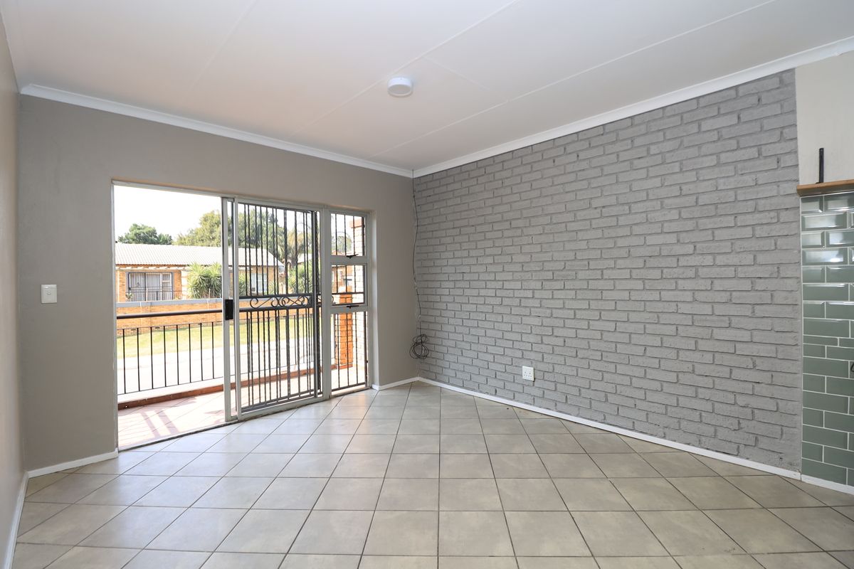 An empty living room featuring tiled flooring, a grey exposed brick feature wall, and a sliding glass door leading to a balcony.
