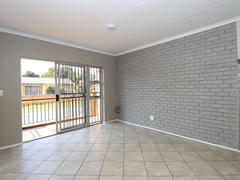 An empty living room featuring tiled flooring, a grey exposed brick feature wall, and a sliding glass door leading to a balcony.