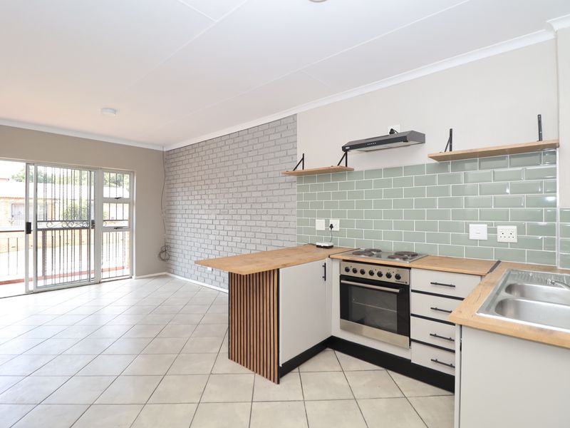 Modern open-plan kitchen and living area featuring a stylish brick accent wall, contemporary cabinetry, wooden countertops, and direct access to a balcony.