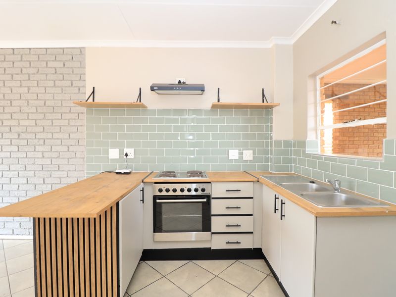 A modern, well-lit kitchen featuring wooden countertops, a subway tile backsplash, built-in oven with hob, and a stylish slatted wood breakfast bar.