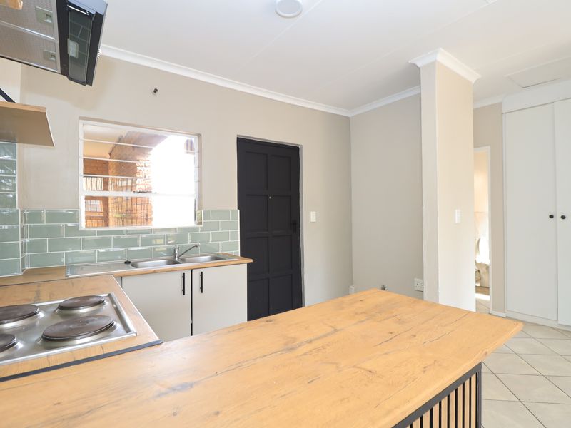 A clean, modern kitchen featuring a wooden countertop, electric hob, extractor fan, subway tile backsplash, and ample built-in storage space.