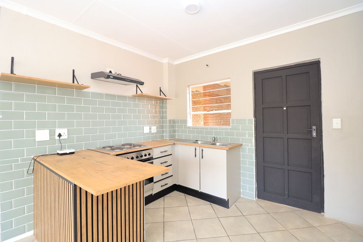 A clean, modern kitchen featuring a subway tile backsplash, wooden countertops, built-in oven with hob, and ample base cabinetry.