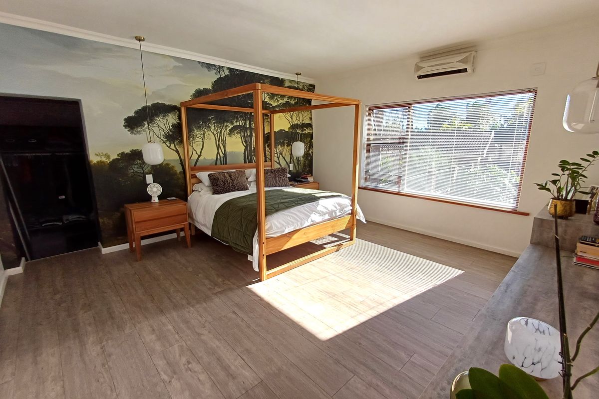 Spacious bedroom featuring wood-look laminate flooring, a large window with venetian blinds, a split-system air conditioner, and a feature wall mural.