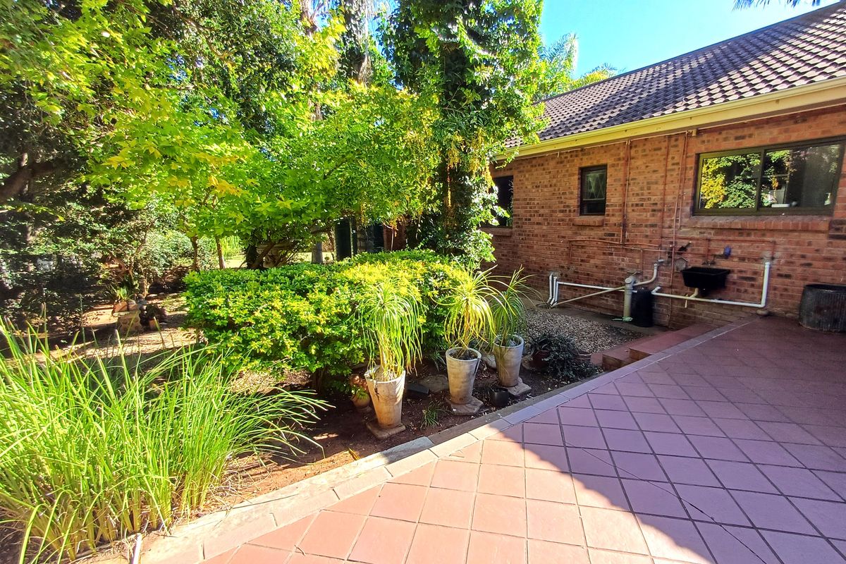 A rear exterior view of the property featuring a brick facade, a tiled patio area, and established garden landscaping.