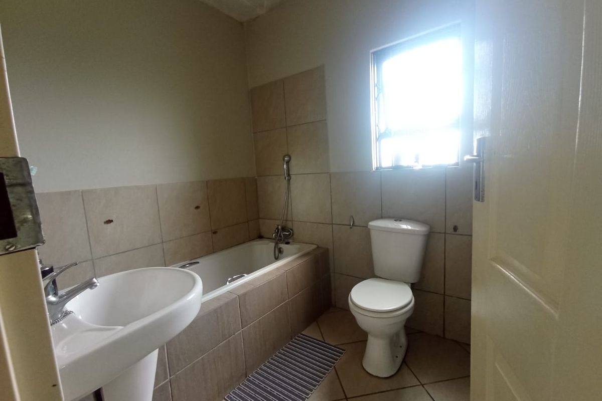 A functional bathroom featuring a pedestal basin, built-in bathtub, and toilet, with neutral wall and floor tiling throughout.
