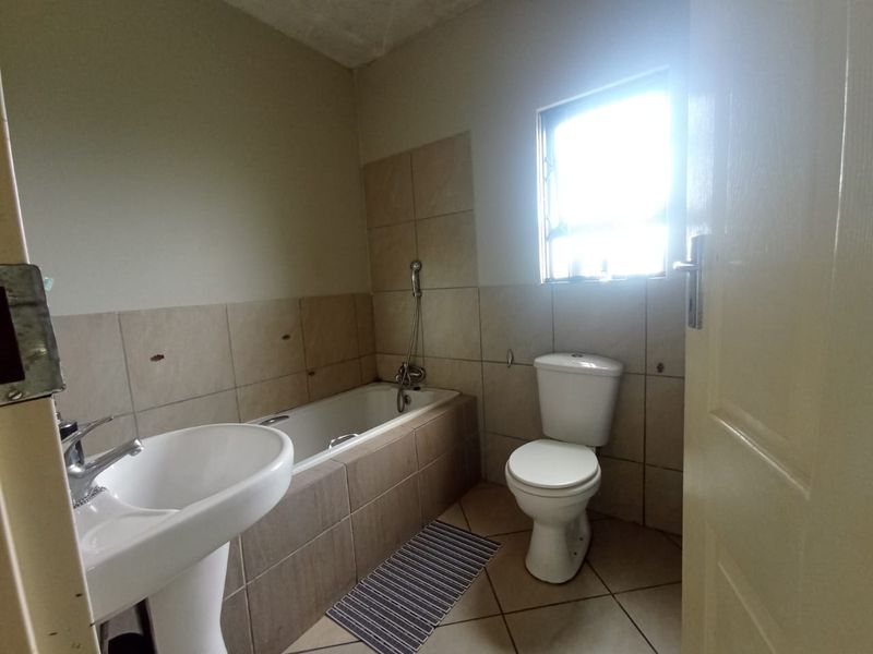 A functional bathroom featuring a pedestal basin, built-in bathtub, and toilet, with neutral wall and floor tiling throughout.
