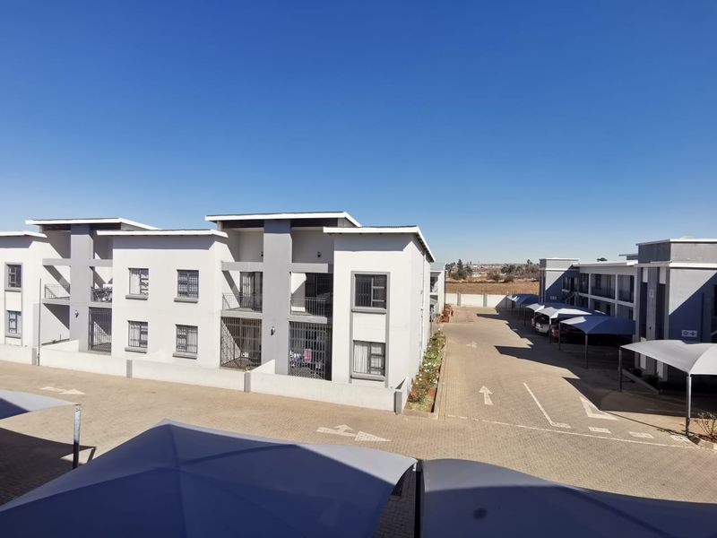 An elevated view of a modern apartment complex featuring paved parking areas, covered carports, and multi-story residential buildings with security features.