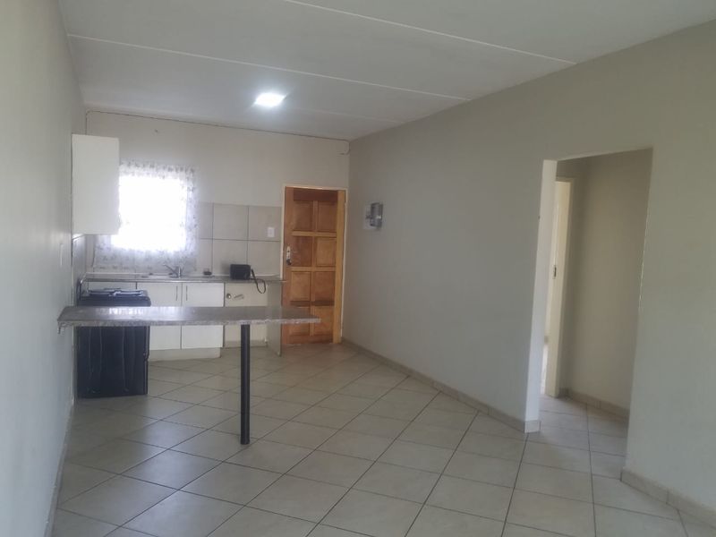 An open-plan living and kitchen area featuring tiled flooring, built-in kitchen cabinetry with a breakfast bar, and neutral wall finishes.