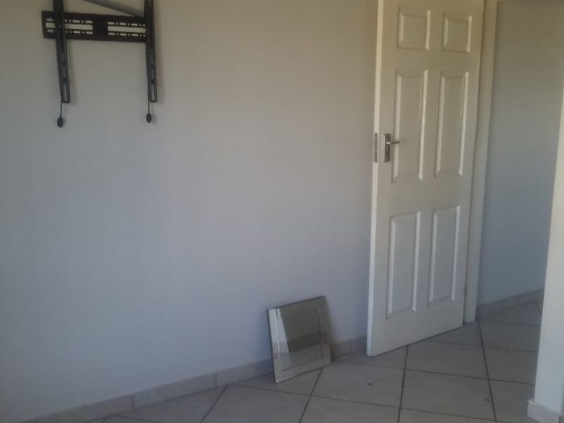 An empty living area featuring neutral wall paint, tiled flooring, and a wall-mounted television bracket.