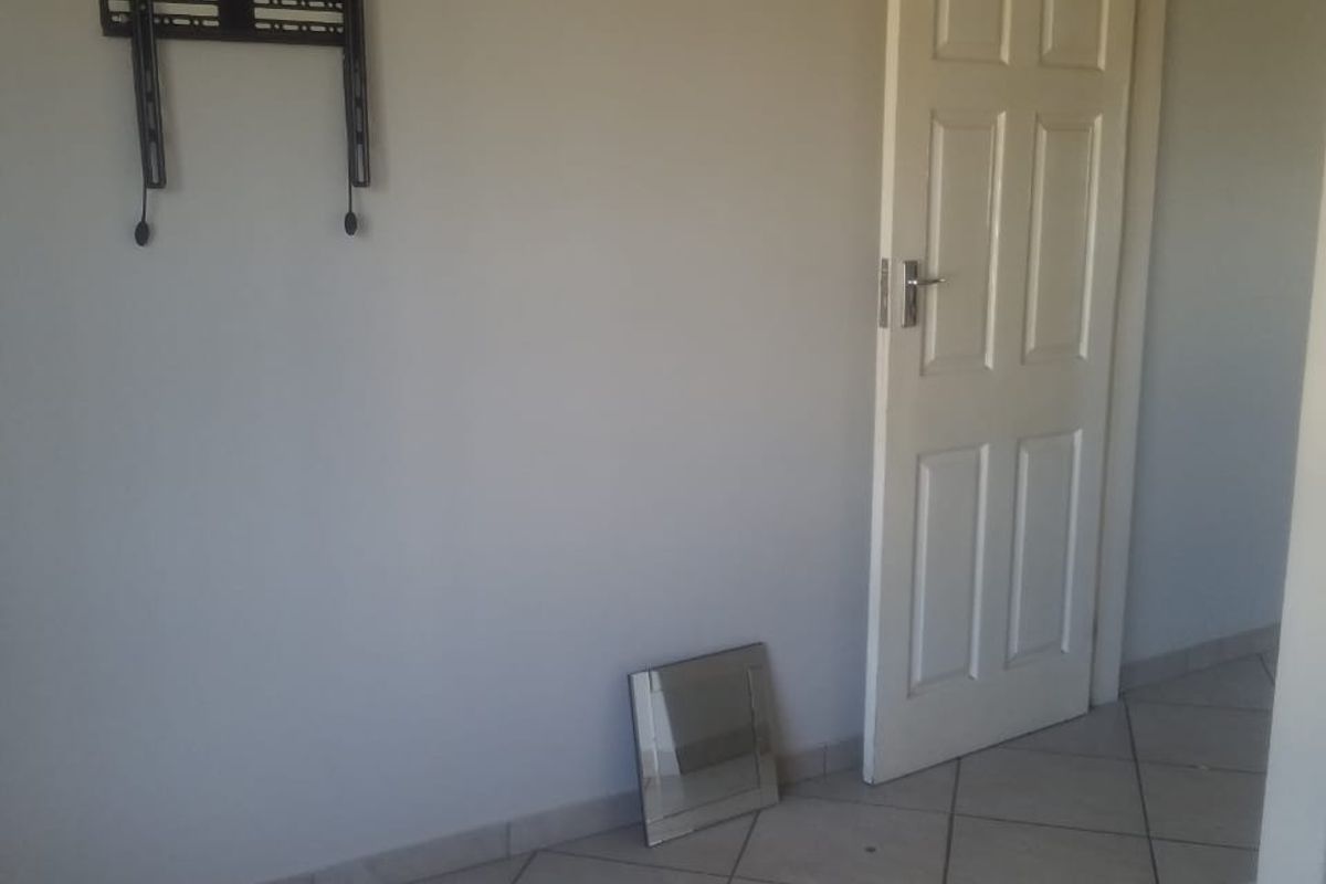 An empty living area featuring neutral wall paint, tiled flooring, and a wall-mounted television bracket.