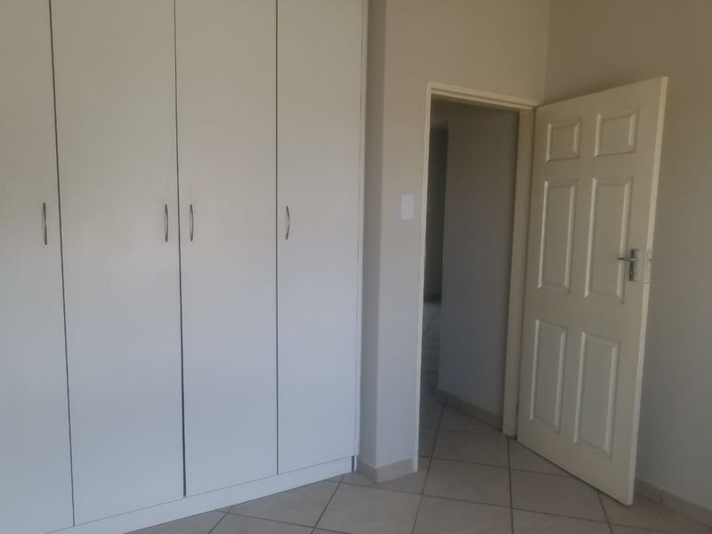 A clean, empty bedroom featuring neutral tiled flooring and ample built-in cupboard storage space.