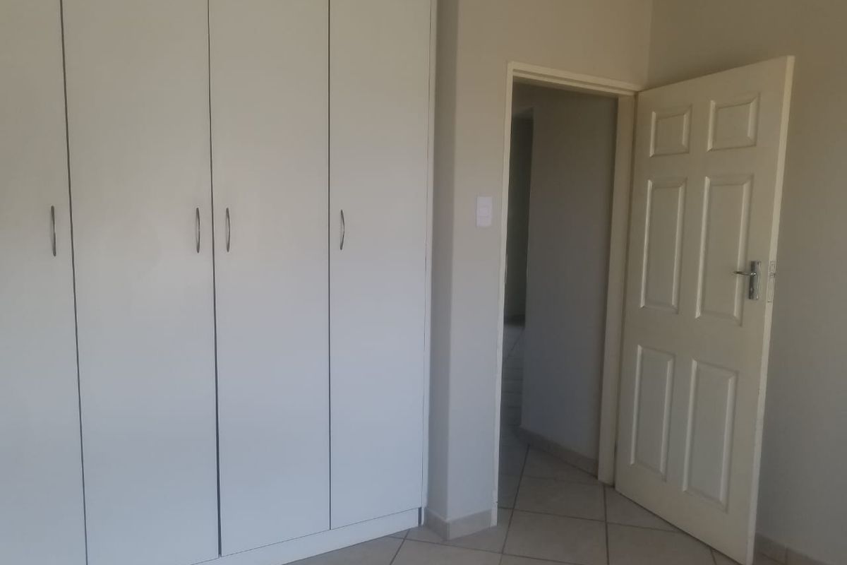 A clean, empty bedroom featuring neutral tiled flooring and ample built-in cupboard storage space.