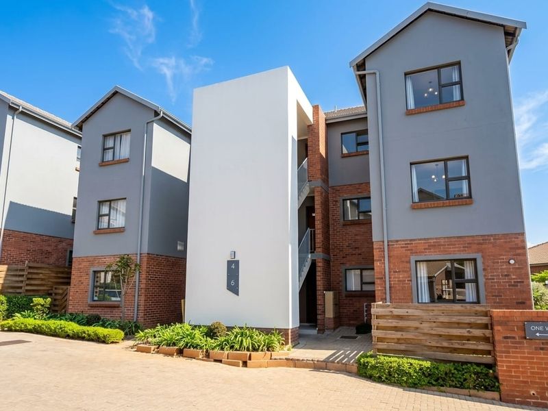 Front elevation of a modern multi-story apartment complex featuring a combination of brick and rendered finishes with paved access and landscaped garden beds.