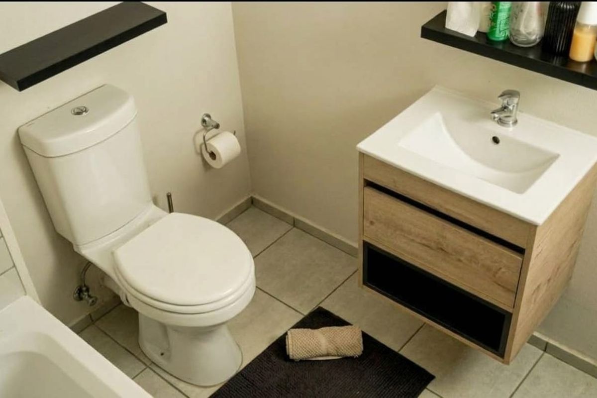 A clean and functional bathroom featuring a modern wood-finish vanity with a ceramic basin, a standard toilet, and floating shelving.