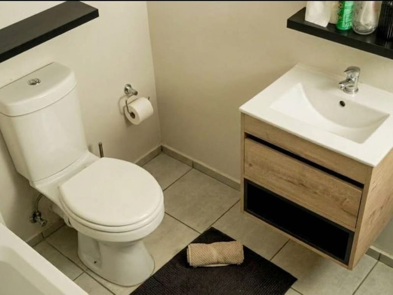 A clean and functional bathroom featuring a modern wood-finish vanity with a ceramic basin, a standard toilet, and floating shelving.