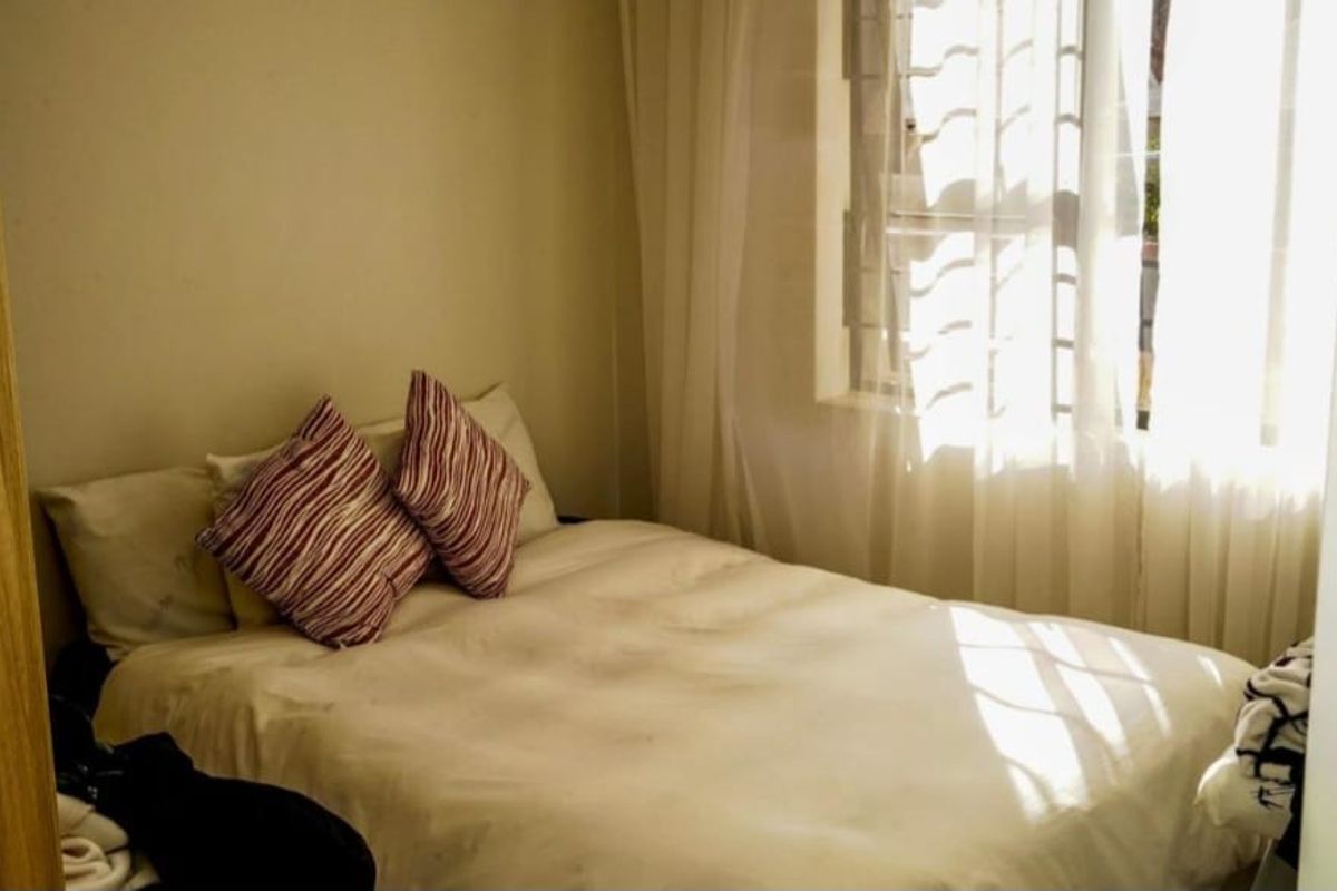 A compact bedroom featuring a built-in wardrobe and a window fitted with security bars, allowing for natural light.