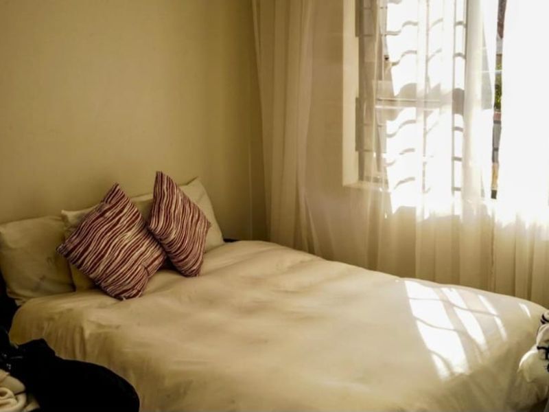 A compact bedroom featuring a built-in wardrobe and a window fitted with security bars, allowing for natural light.